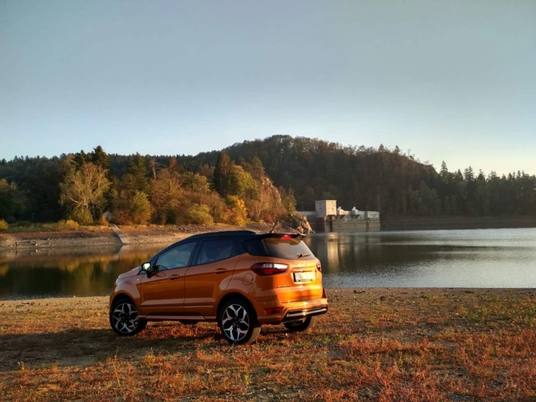Oranžový Ford EcoSport zaparkovaný u jezera s lesním pozadím.