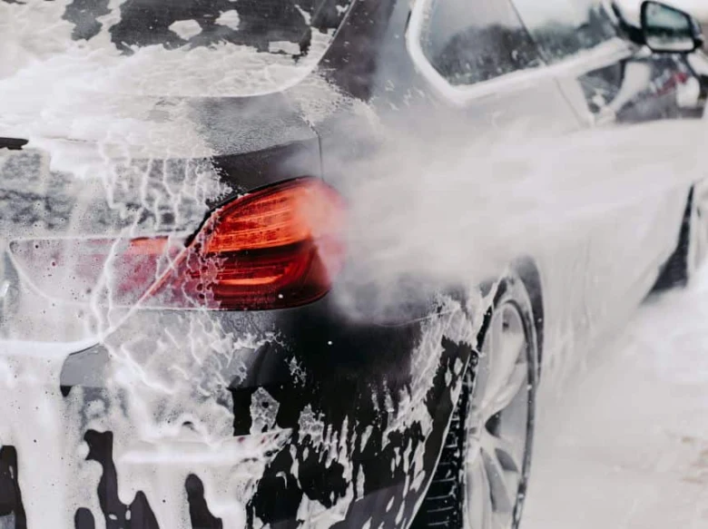 Černé auto pokryté mýdlovou pěnou při mytí.