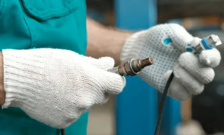 Mechanik drží svíčku a senzor kyslíku při opravě motoru.