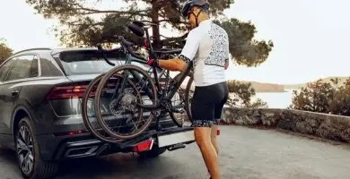 Muž připevňuje kolo na zadní nosič automobilu.