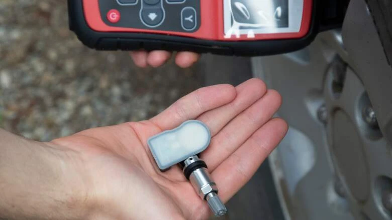 Ruka drží snímač tlaku v pneumatikách s diagnostickým přístrojem.