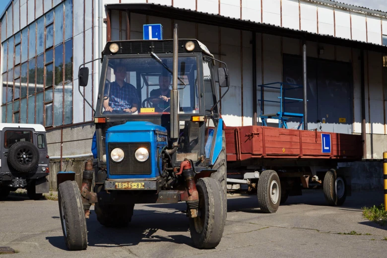 Modrý traktor s přívěsem před budovou ukazuje praktické použití.