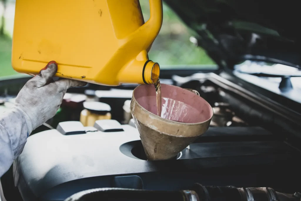 Mechanik nalévá olej do motoru auta při údržbě.