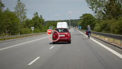 Červený osobní automobil jedoucí po dálnici s cyklistou vpravo.