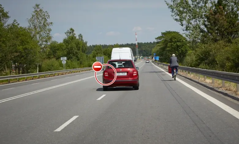 Červený osobní automobil jedoucí po dálnici s cyklistou vpravo.