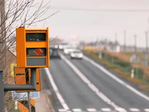 Žlutý semafor na silnici s auty v pozadí.