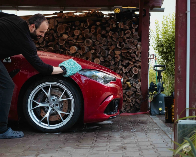 Muž umývá červené auto po lakování s houbou.