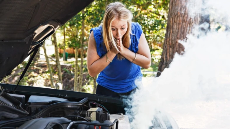 Žena se dívá na kouřící motor auta venku.
