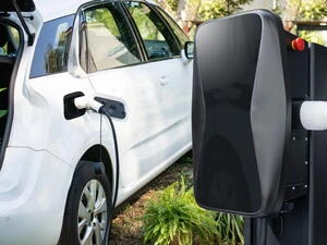 Bílý elektromobil nabíjen na venkovní stanici.