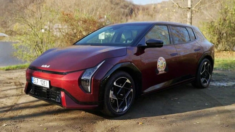 Červený crossover Kia EV6 zaparkovaný na zemi před stromy.