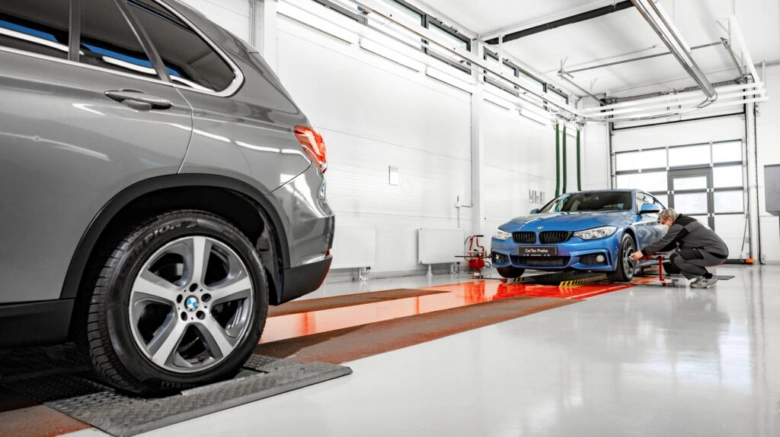 Mechanik opravuje modrého BMW v dílně vedle šedého SUV.