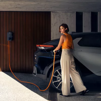 Žena nabíjí elektromobil v garáži pomocí kabelu.