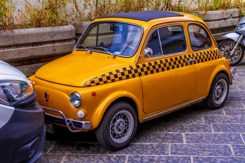 Žluté starožitné taxíkové auto s černobílými proužky.