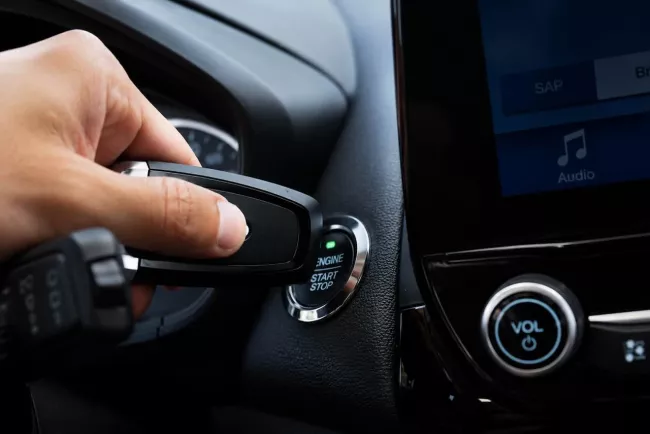 Ruka s klíčem u tlačítka Start/Stop v autě Toyoty.