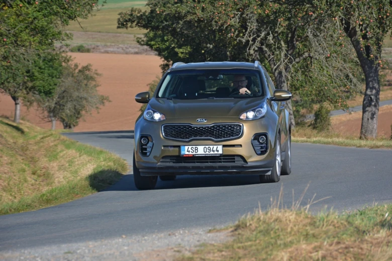 Bronzový Kia Sportage páté generace jede po venkovské silnici.