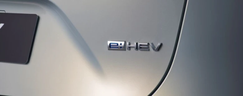 Detailní záběr na stříbrné logo e:HEV na zadním nárazníku auta.