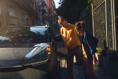 Muž nabíjí elektromobil s dítětem na ulici.