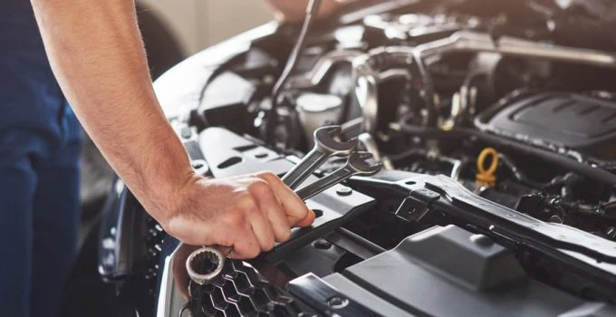 Mechanik opravuje auto pod kapotou s klíčem v ruce.