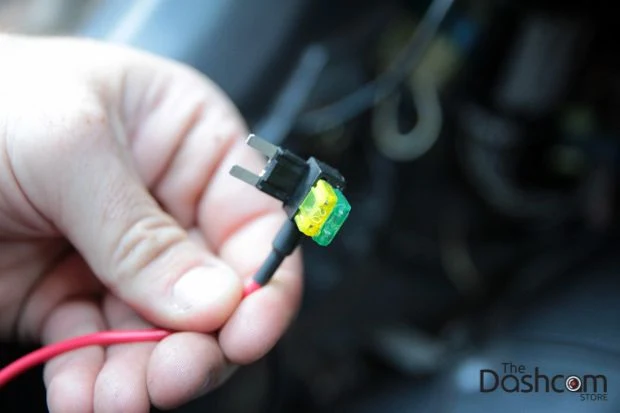 Ruka drží pojistku s červeným kabelem pro instalaci USB portu v autě.