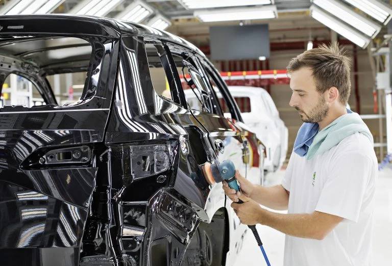 Pracovník v továrně lakuje černé auto bruskou.