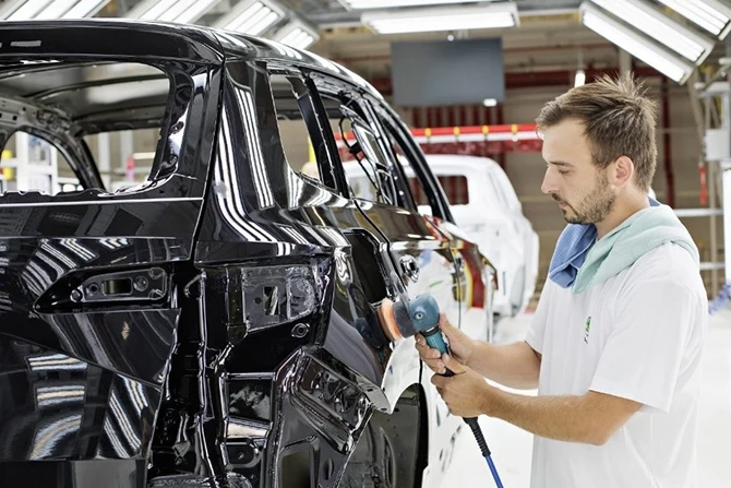 Pracovník lakuje černý automobil v továrně.