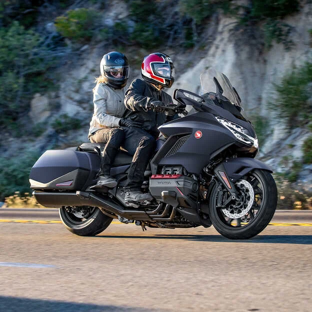 Černá motorka s dvěma jezdci na silnici.