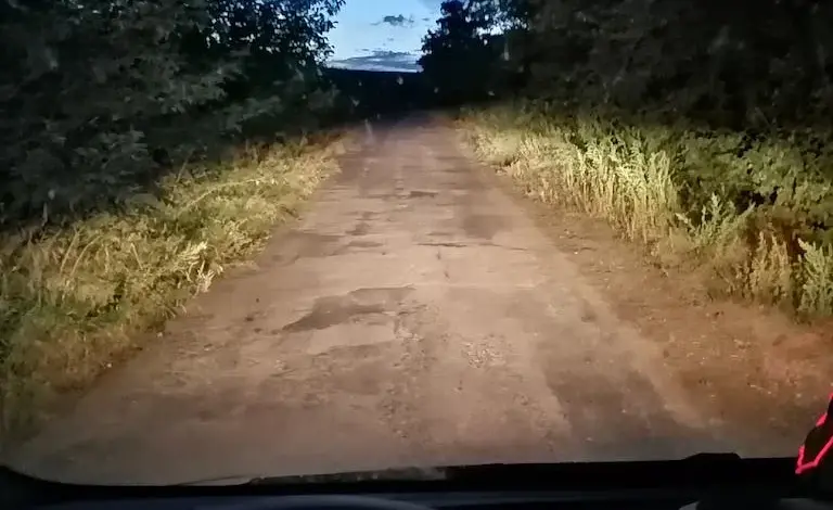 Vnitřní pohled z auta s rozsvícenými světly na nezpevněné cestě.