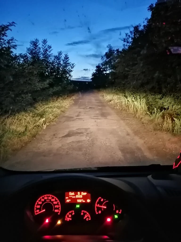 Vnitřní pohled z auta s rozsvícenými světly na nezpevněné cestě.