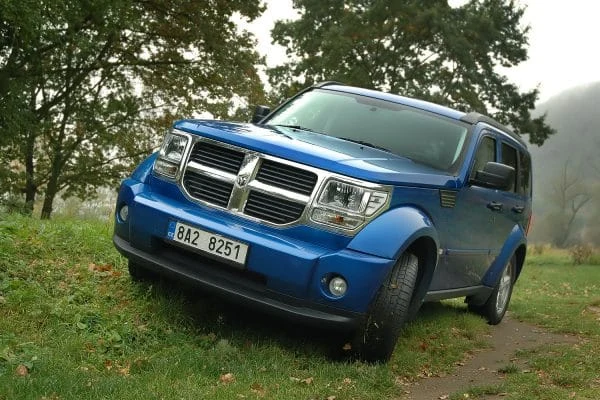 Modrý SUV automobil Dodge Nitro na trávě mezi stromy.