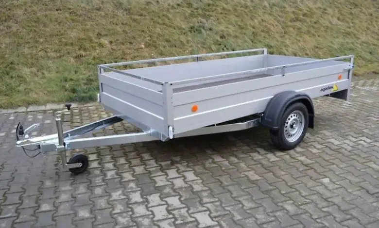 Stříbrný přívěs s otevřeným nákladním prostorem na dláždění.