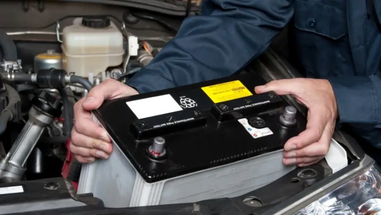 Mechanik drží autobaterii s viditelnými nádržemi na vodu pod kapotou auta.
