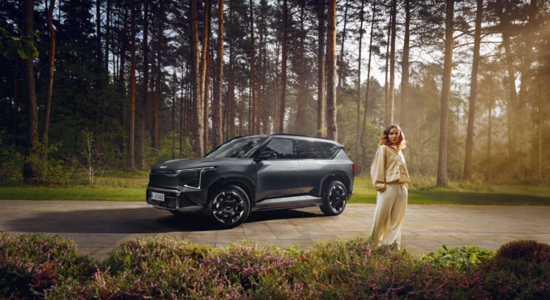 Tmavý SUV Kia Sportage stojí na cestě v lese s ženou.